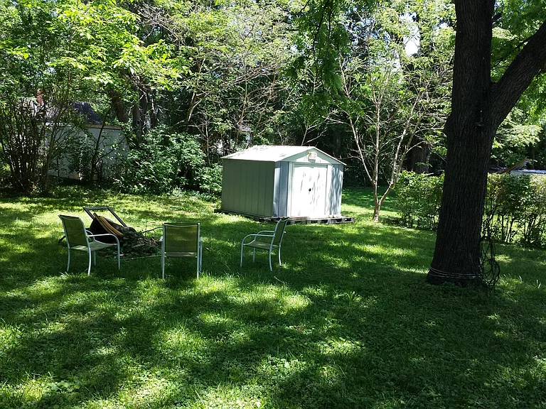 Shady back yard with storage she for tools and 'stuff'.