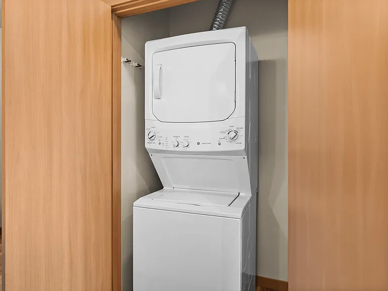 Compact in-unit laundry area with modern stacked washer and dryer, neatly tucked behind wooden doors. Compact in-unit laundry area with modern stacked washer and dryer, neatly tucked behind wooden doors.