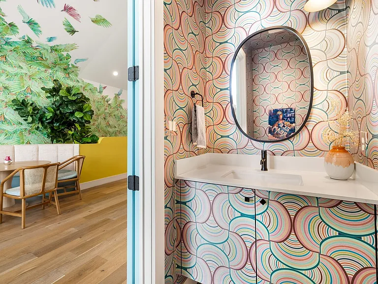 Powder room featuring a patterned wallcovering, oval mirror, single vanity with integrated sink, and dark-finish faucet