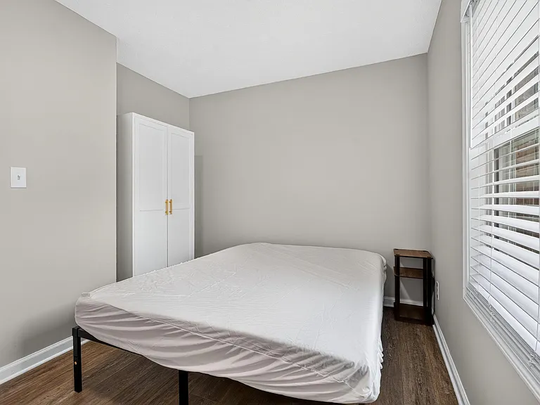 Private bedroom with large window and blinds, wood-look flooring, and a wardrobe closet for convenient storage.