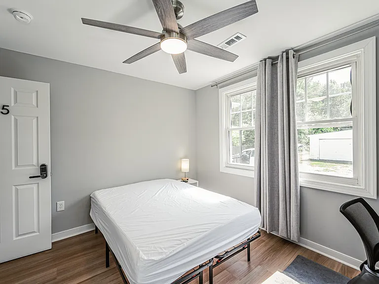 Private bedroom with a large window, ceiling fan, and space for a bed plus a small desk setup.