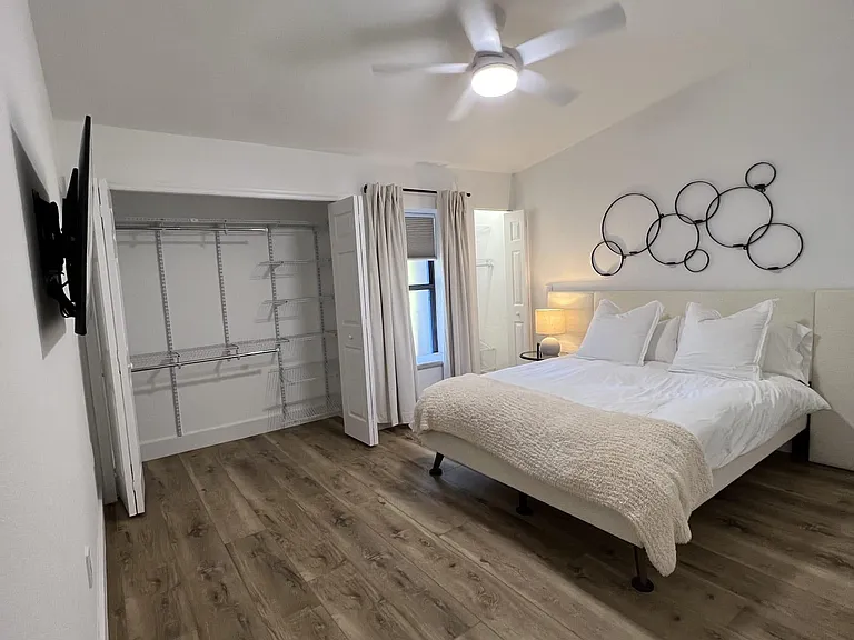 Spacious bedroom with a ceiling fan, wood-look flooring, and a large open closet with built-in shelving for easy storage.