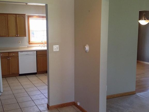 Standing in entry, view of tiled entry hall and kitchen, dining room with hardwood floor, and carpeted living room. Paint on all walls are a shade of beige.