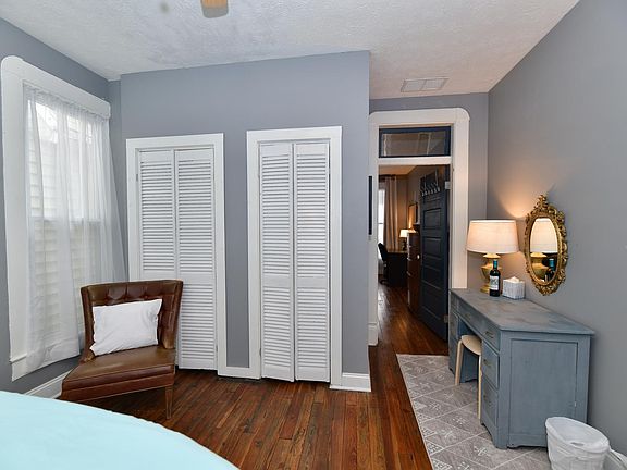 The master bedroom has an oversized chair and vanity inside the room. There is also a ceiling fan.