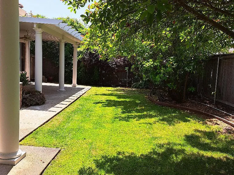 Large covered patio, shaded yard with artificial turf