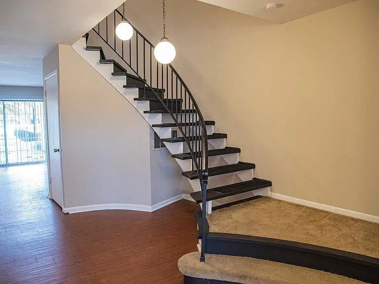Inviting interior featuring a modern spiral staircase with elegant lighting, leading to a bright living area with stylish wood flooring and sliding glass doors.