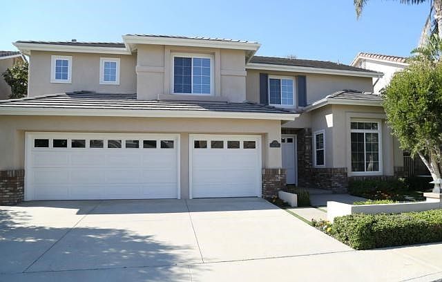 Front of home showing 3 car garage and driveway as well as gutters and brick trim and cement tile roof