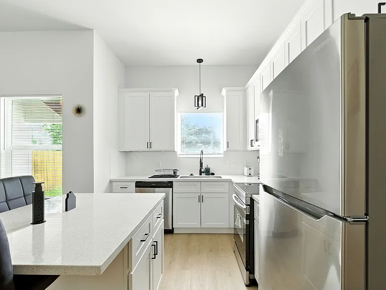 Galley-style kitchen with white shaker cabinets, quartz counters, stainless appliances, and a peninsula for seating.