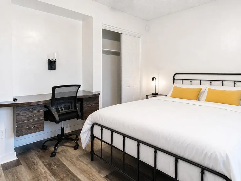 Furnished bedroom with a full bed, dedicated work desk, and an open closet with shelving for easy storage.
