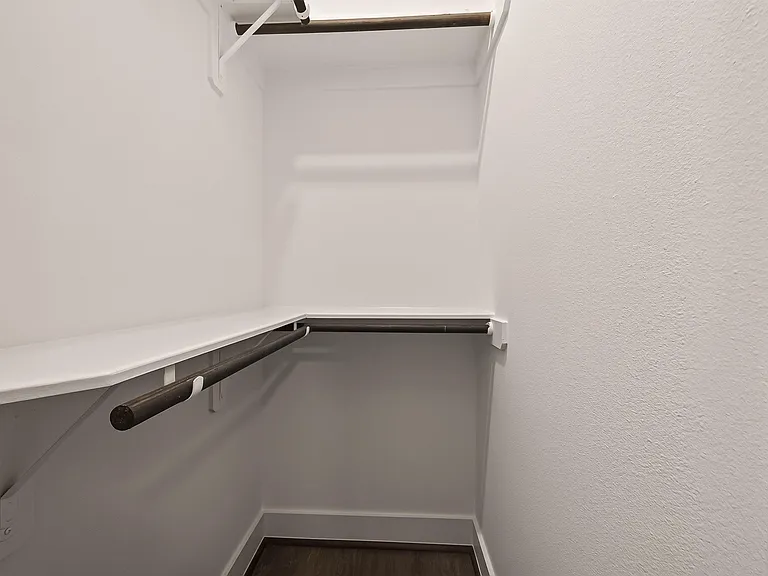 Walk-in closet with dual hanging rods and wraparound shelving for organized clothing and extra storage.
