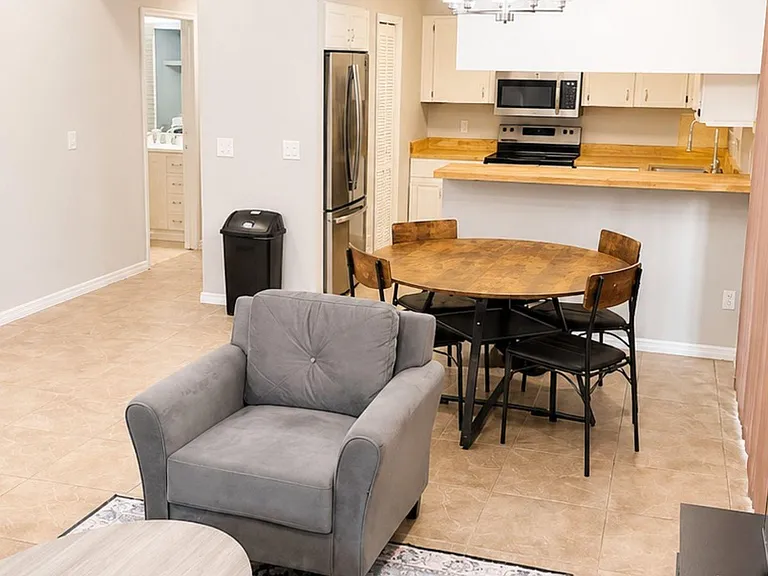 Open-concept common area with dining table, comfortable seating, and an adjoining kitchen with breakfast bar and stainless ap