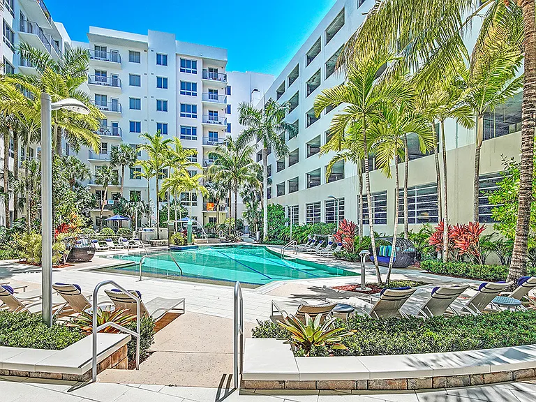 Luxury apartment resort-style pool with palm trees, sun loungers, and landscaped courtyard