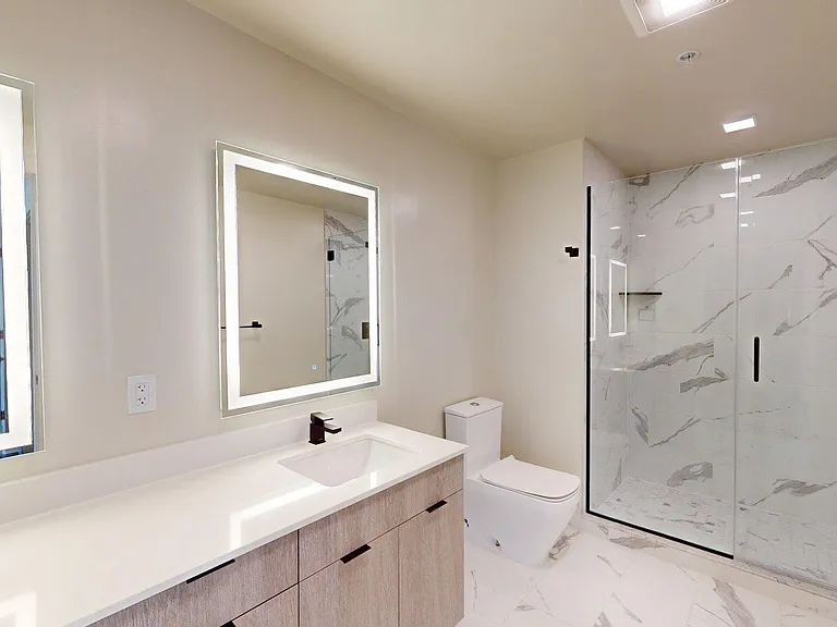 Apartment bathroom with glass-enclosed shower, wood-style flooring, double sinks, and LED vanity mirror.