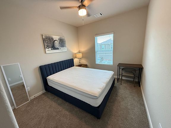 Furnished bedroom with a full bed, nightstand, ceiling fan, and a dedicated desk space near the window.