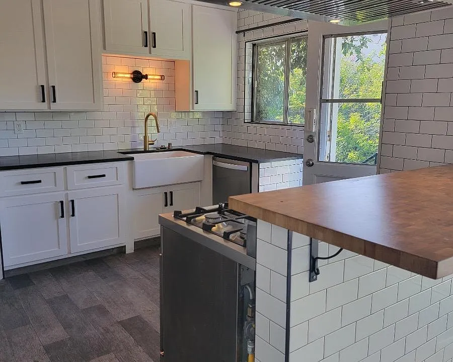 Remodeled kitchen with butcher block pass through to dining room and stainless hood over the stove. Tile floor white cabinets with decorator handles and light fixtures.