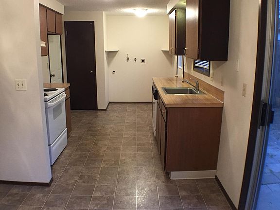 Galley style kitchen with electric range and dishwasher. Rear wall has washer and dryer hookups and the door is a pantry.