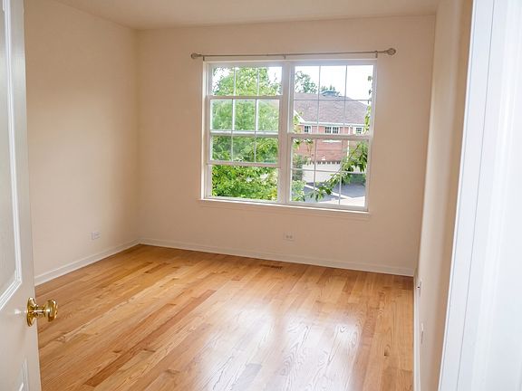 First bedroom featuring hardwood floors and natural light from a window overlooking the tree lined driveway.