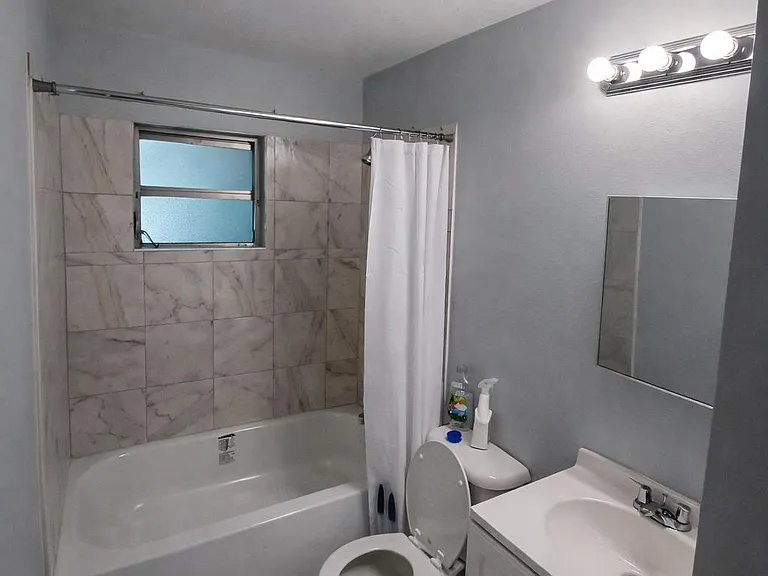 Full bathroom with tub/shower surround, tiled floors, vanity sink, and a privacy window for ventilation and light.