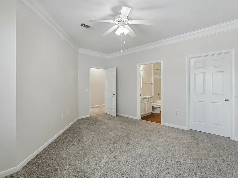 Bright spacious bedroom with plush carpet, featuring a ceiling fan and en-suite bathroom access. Bright spacious bedroom with plush carpet, featuring a ceiling fan and en-suite bathroom access.
