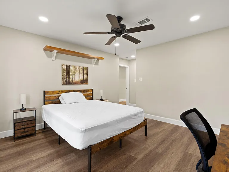 Spacious bedroom with wood-look flooring, ceiling fan, nightstands, and a dedicated desk area for working or studying.