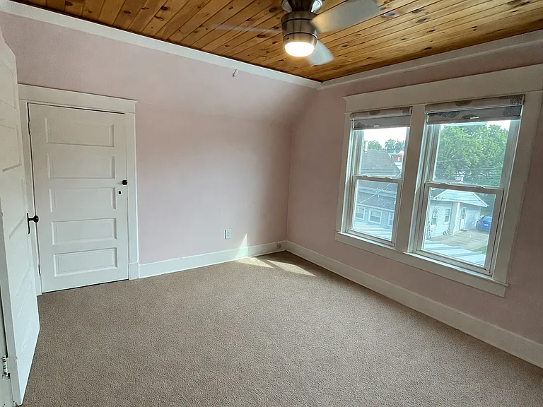 Spacious upstairs bedroom with natural light and warm wood ceiling accent.