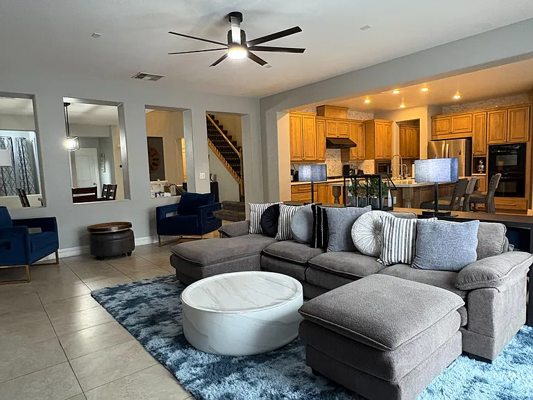 Open-concept living area with sectional seating, ceiling fan, and direct sightlines to the kitchen with breakfast bar.