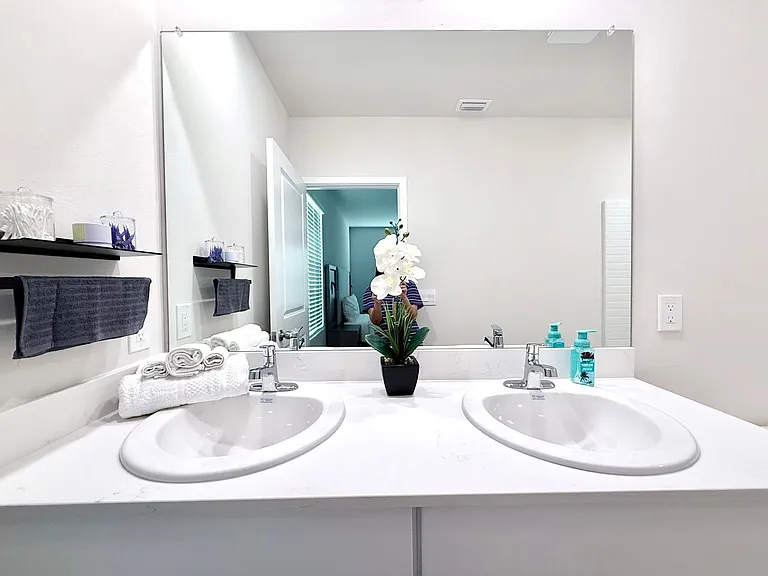 Double-sink vanity with wide countertop, large wall mirror, and open shelving for everyday bathroom storage.