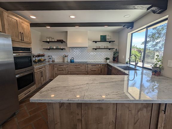 Remodeled kitchen with view of back patio, quartzite countertops, double oven, and cooktop hood.