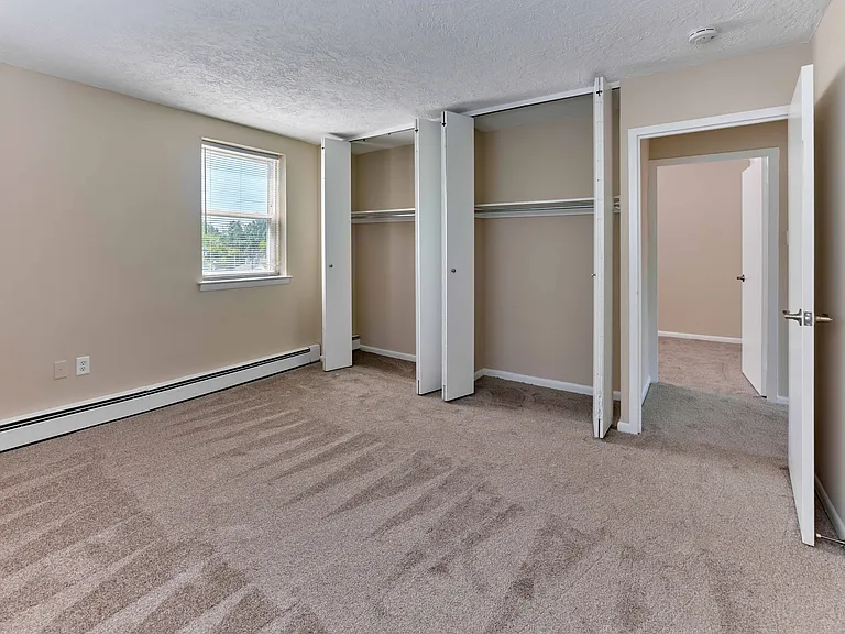 Spacious carpeted bedroom with dual closets and bright natural light at Audubon Arms Apartments.