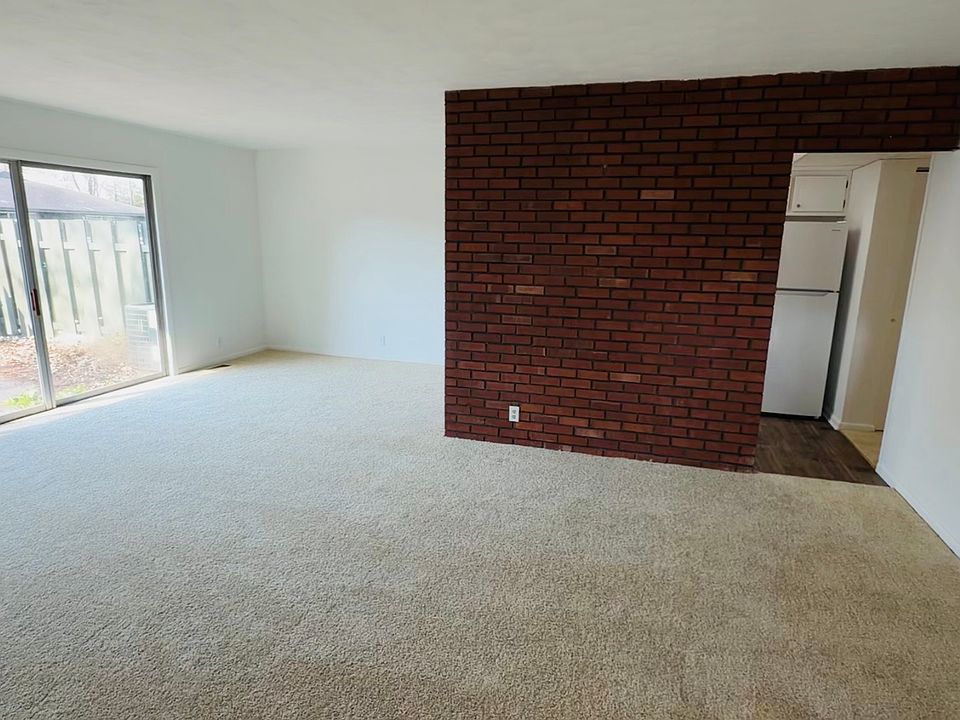 Spacious living room featuring a brick accent wall with adjoining kitchen