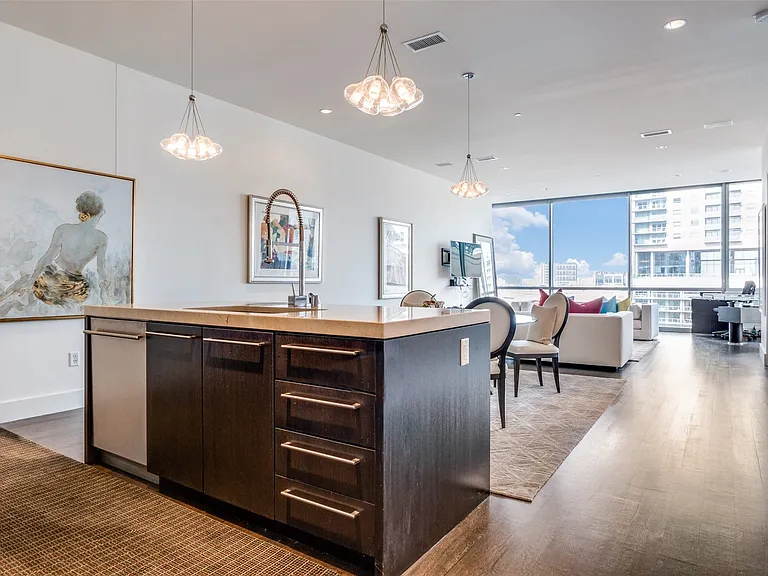 Kitchen with dark brown cabinetry, hanging light fixtures, light countertops, an island with sink, and open floor plan