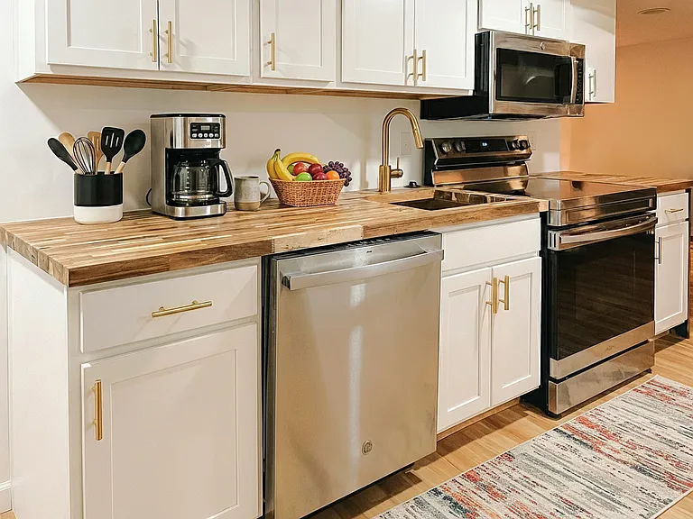 Updated kitchen with white cabinetry, stainless steel appliances, modern hardware, and warm wood-style flooring.