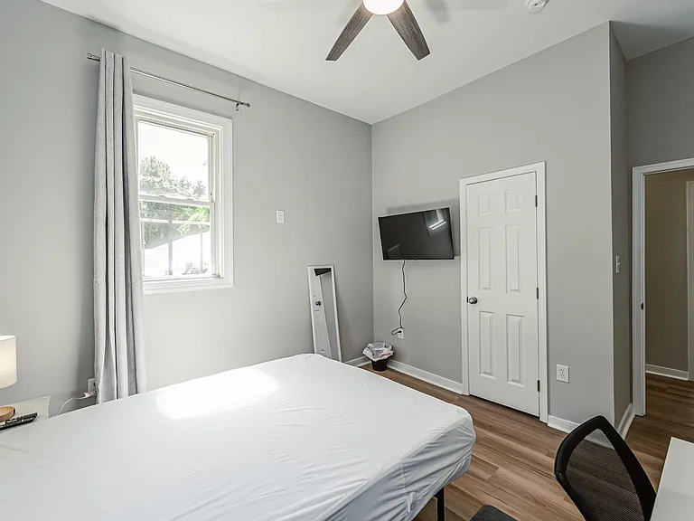 Comfortable bedroom featuring a large window with curtains, ceiling fan, and space for a full bed plus a small desk setup.
