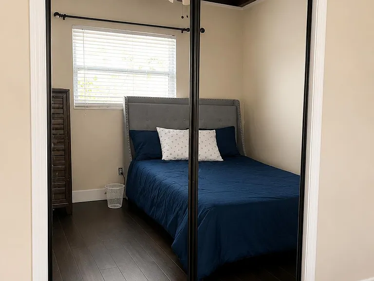 Bedroom offers a full-size bed setup, hardwood floors, a window with blinds, and mirrored sliding closet doors.