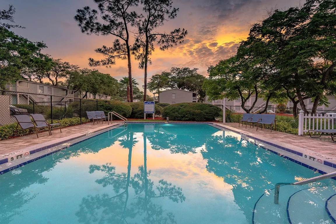 Inviting residential pool area with lounge chairs and lush greenery, set against a stunning sunset sky.