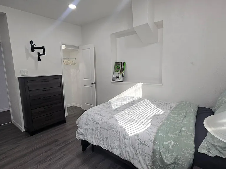 Private furnished bedroom with a full bed, dresser, and open closet storage, plus easy access to nearby hallway space.