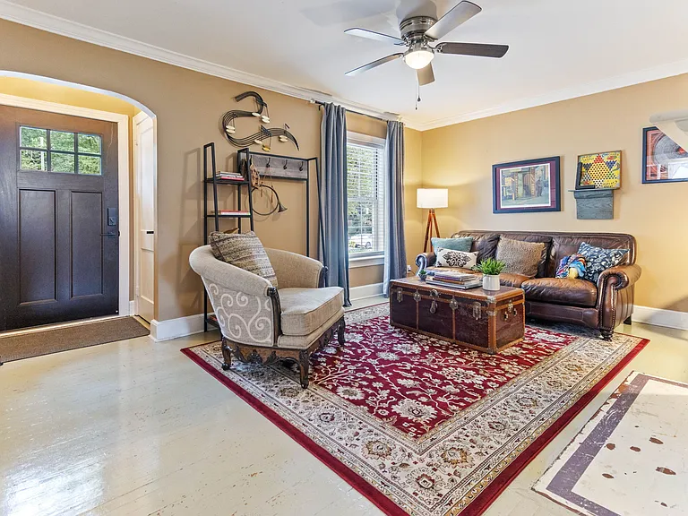 Cozy living room at Hunsucker's Place near Downtown Greensboro, featuring a comfortable leather couch, a functional writing desk, and an open-concept design connecting to the dining room with a piano and the fully equipped kitchen_perfect for relaxation