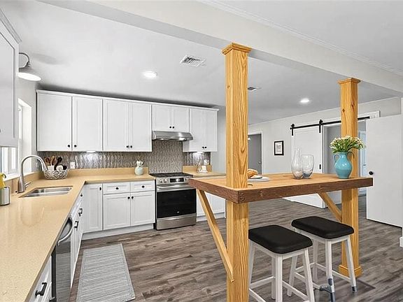 Kitchen featuring decorative columns, dark wood finished floors, visible vents, under cabinet range hood, and stainless steel appliances