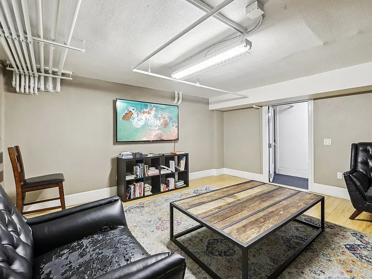 Room with a wooden coffee table surrounded with armchairs, bookshelf, and a flat-screen TV