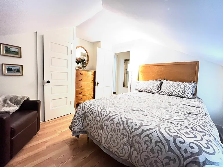Queen sized mattress in private bedroom, small recliner chair, closet and dresser.