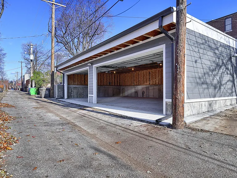 Interior garage view shows generous parking space, tall overhead doors, interior lighting, and convenient alley access.