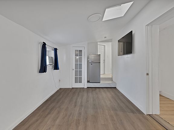 Unfurnished living room with vaulted ceiling with skylight, baseboards, and wood finished floors