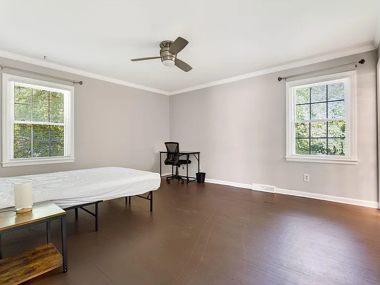 Spacious bedroom with two large windows, ceiling fan, and durable wood-look flooring, plus room for a desk setup.