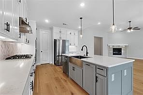 Kitchen with white cabinetry, light wood-style floors, light countertops, a center island with sink, and recessed lighting