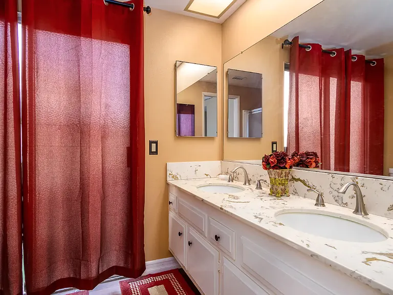 This is the bathroom in the owner 's suite. It has he/she sinks, a sliding door for natural lighting which leads to the sideyard garden. It has a shower.