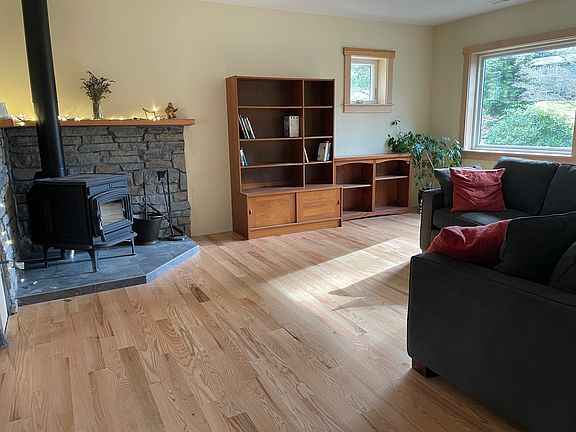 Large living room with new Oak flooring, hearth, and south and west facing windows. This is just off the kitchen. Your choice of available furnishings, including sectional couch.