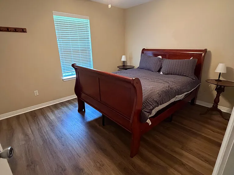 Furnished bedroom with a sleigh bed, wood-style flooring, window with blinds, and a ceiling fan with light.