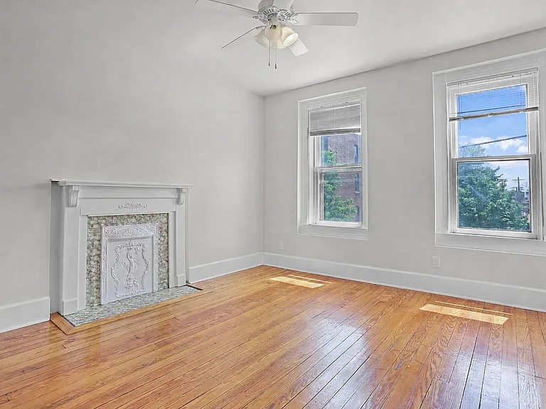 Bedroom with salvaged hardwood floors, tall windows, decorative mantel, and charming historic trim.