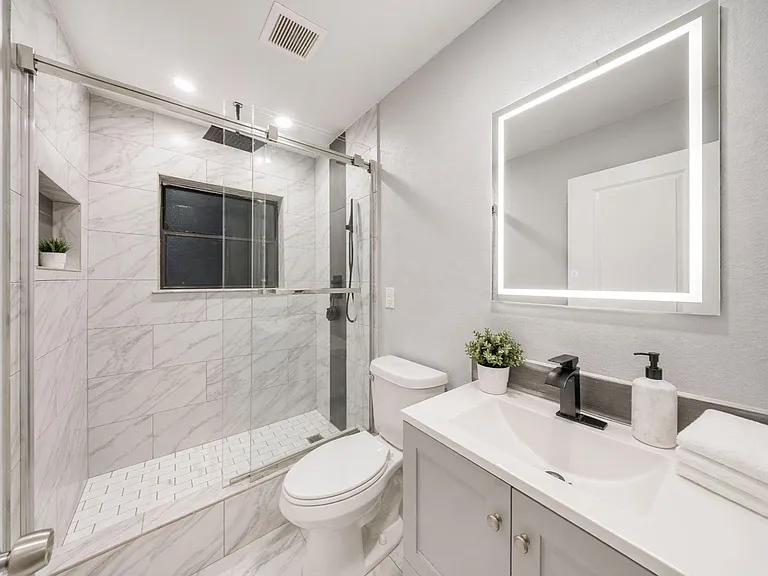 Updated bathroom with a glass-enclosed tiled shower, sleek vanity with undermount sink, and illuminated mirror.