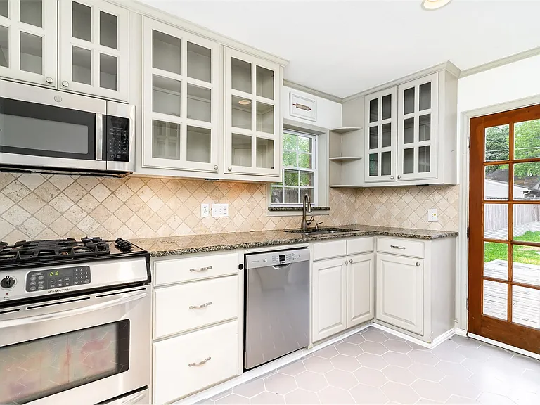 Kitchen with stainless steel appliances, open shelves, a sink, stone counters, and tasteful backsplash